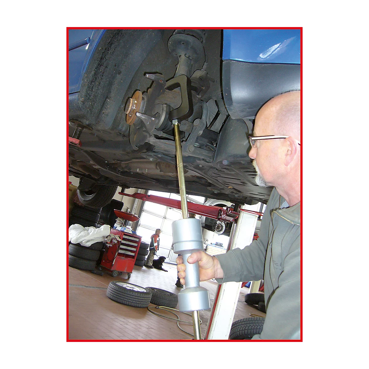 Ein Mechaniker inspiziert das Fahrwerk eines Autos. Er hält ein Werkzeug und steht unter dem Fahrzeug.